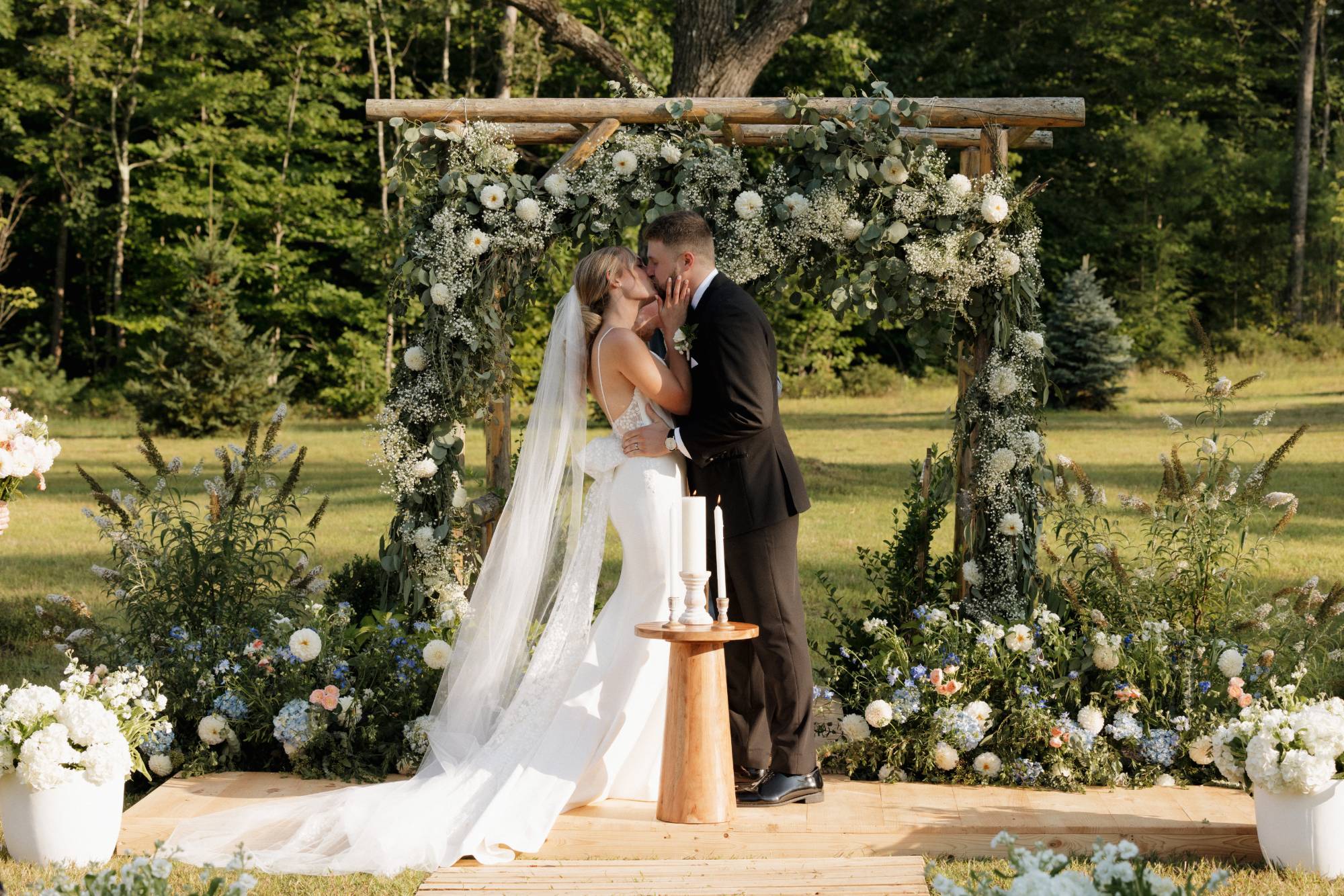 A ceremony kiss beneath a wooden arch draped in eucalyptus and white dahlias