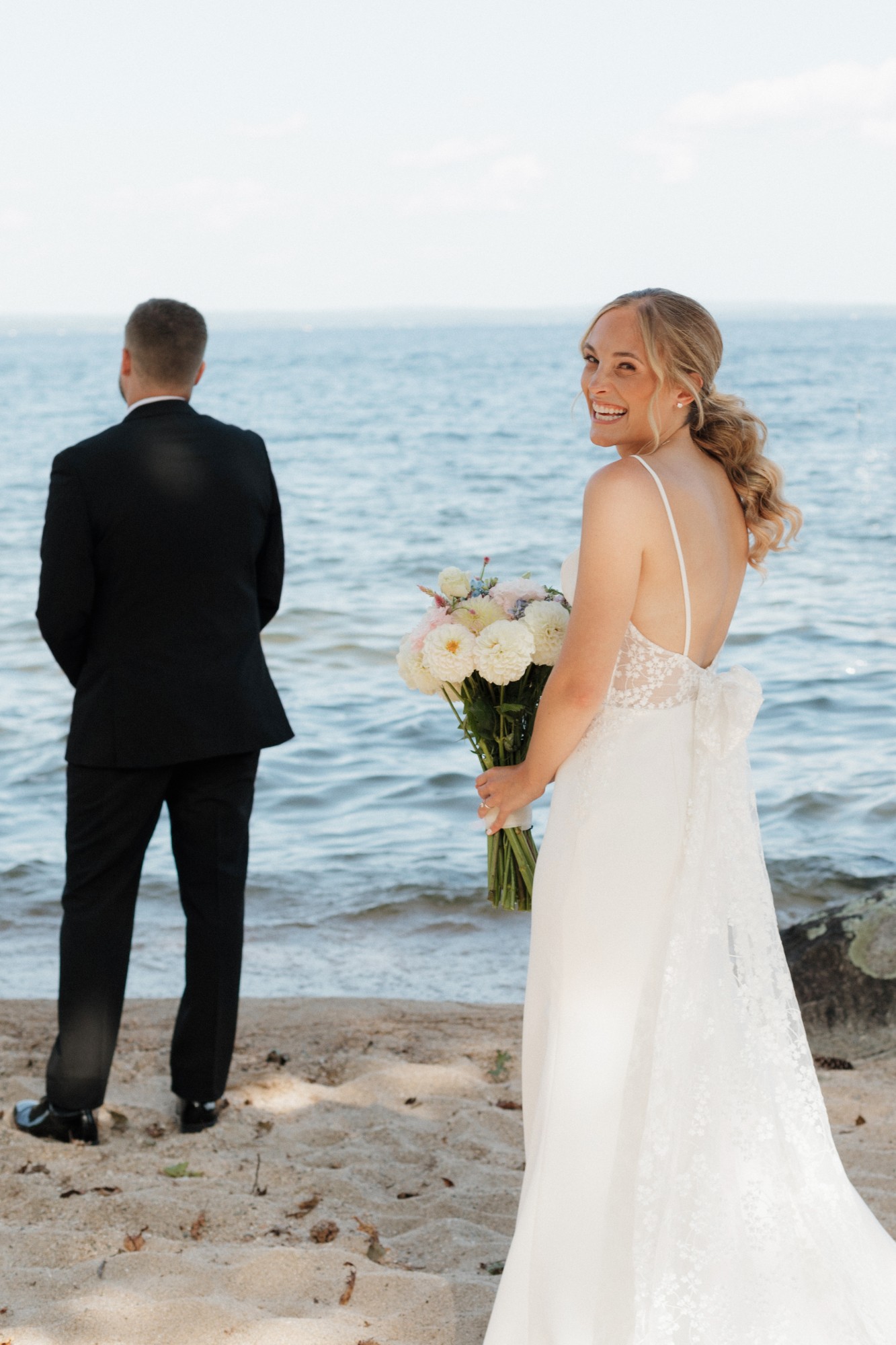 Bride glancing back with her bouquet before the first look at the water's edge